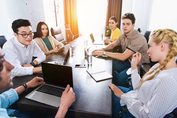 Immagine ritagliata di partner commerciali multiculturali che si riuniscono a tavola con computer portatili in ufficio moderno — Foto stock