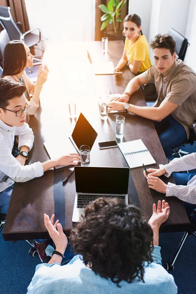 Visão de alto ângulo de parceiros de negócios multiculturais que têm reunião à mesa com laptops no escritório moderno — Fotografia de Stock