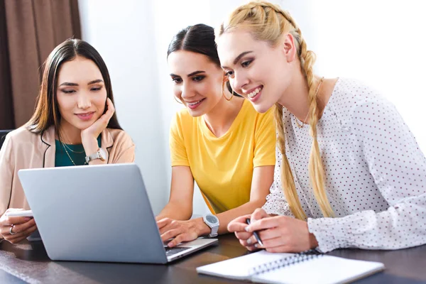 Tres mujeres de negocios multiculturales que utilizan el ordenador portátil en la mesa en la oficina moderna - foto de stock