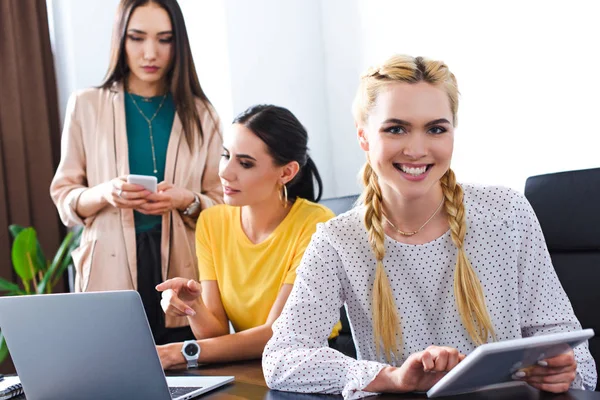 Sorridente empresária com tablet digital e seus colegas para trás no escritório moderno — Fotografia de Stock