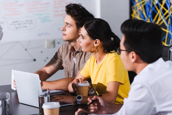 Socios comerciales multiculturales que se reúnen en la mesa con ordenadores portátiles en la oficina moderna - foto de stock