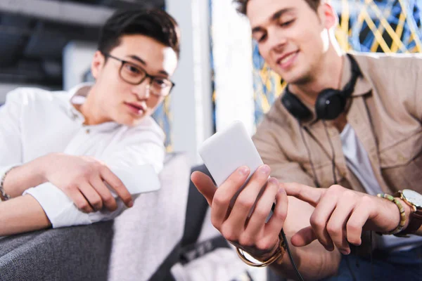 Businessman showing smartphone screen to asian colleague at modern coworking office — Stock Photo