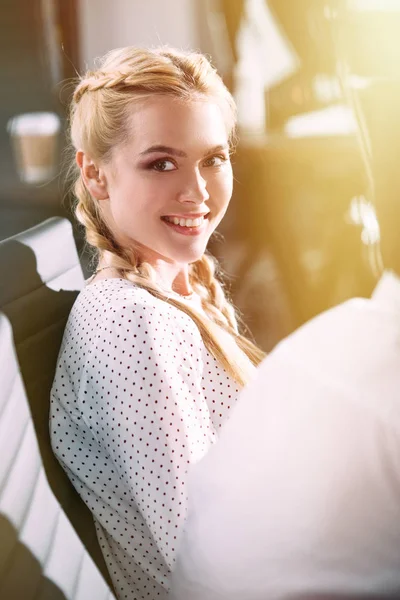 Smiling young businesswoman sitting on chair and looking at camera in modern office — Stock Photo