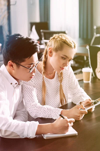 Junge asiatische Geschäftsfrau schreibt in Lehrbuch und Geschäftsfrau nutzt digitales Tablet im modernen Büro — Stockfoto