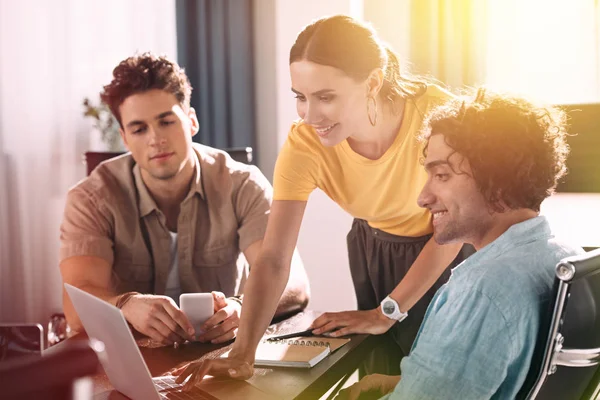 Lächelnde Geschäftsfrau mit Laptop, während zwei Geschäftsleute im modernen Büro am Bildschirm zuschauen — Stockfoto