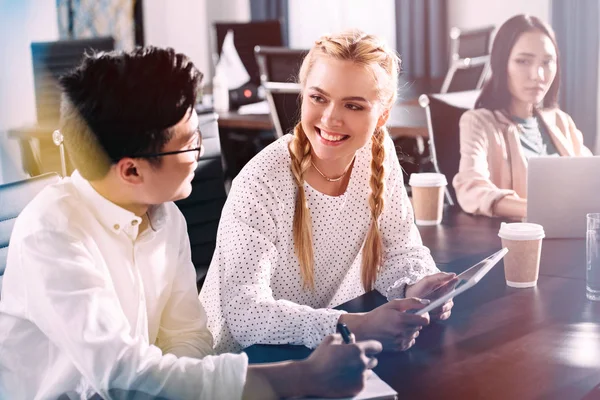 Young asian businessman writing in textbook and talking to businesswoman with digital tablet at modern office — Stock Photo