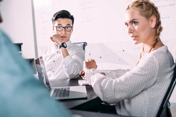 Joven asiático hombre de negocios y mujer de negocios sentado a la mesa con portátil durante la reunión de negocios en la oficina moderna - foto de stock