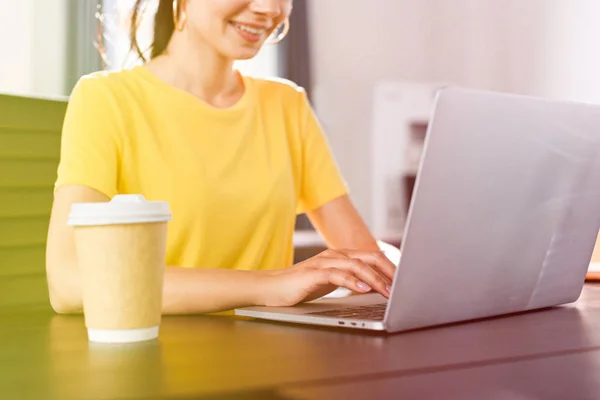 Imagem recortada de mulher de negócios sorridente sentado à mesa com laptop e xícara de café no escritório moderno — Fotografia de Stock