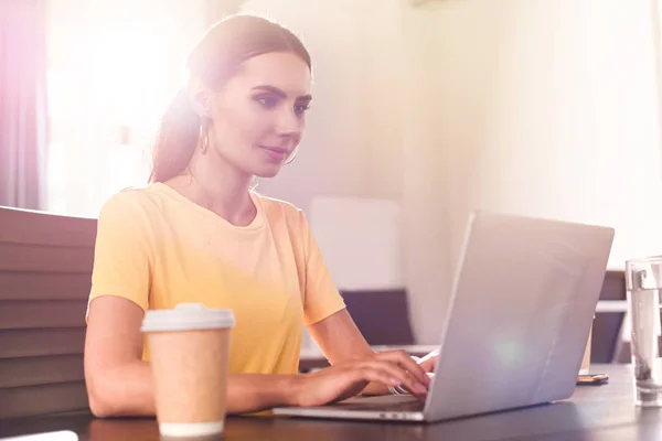 Junge Geschäftsfrau tippt auf Laptop am Tisch mit Pappbecher Kaffee im modernen Büro — Stockfoto