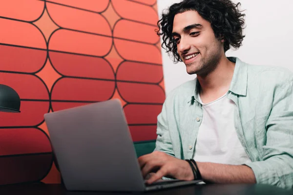 Sonriente joven hombre de negocios sentado en la mesa con el ordenador portátil en la oficina moderna - foto de stock