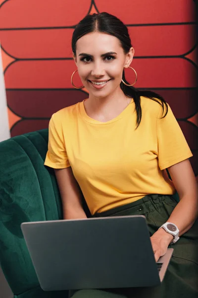 Улыбающаяся молодая деловая женщина, сидящая с ноутбуком в современном офисе — стоковое фото