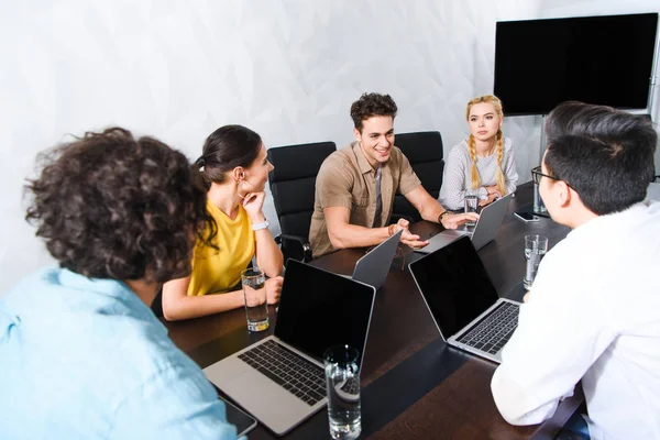 Grupo de empresarios multiculturales discutiendo en la mesa con ordenadores portátiles en la oficina moderna - foto de stock