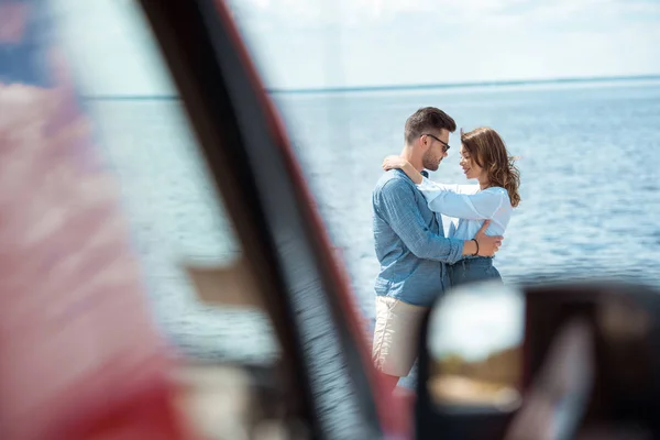 Вибірковий фокус автомобіля і молода пара охоплює біля моря — стокове фото