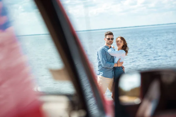 Selective focus of car and young couple hugging near the sea — Stock Photo
