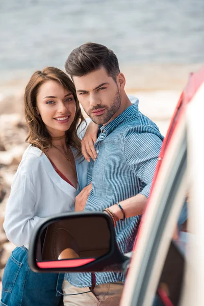 Lächelndes junges Paar, das sich im Urlaub in der Nähe seines Autos umarmt — Stockfoto