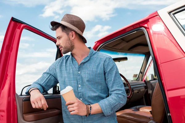 Homem elegante com copo descartável de café de pé no carro durante a viagem de carro — Fotografia de Stock