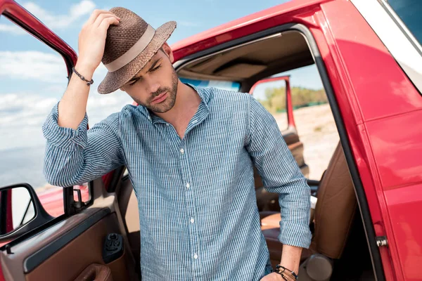 Schöner stylischer Mann mit Hut steht neben rotem Auto — Stockfoto