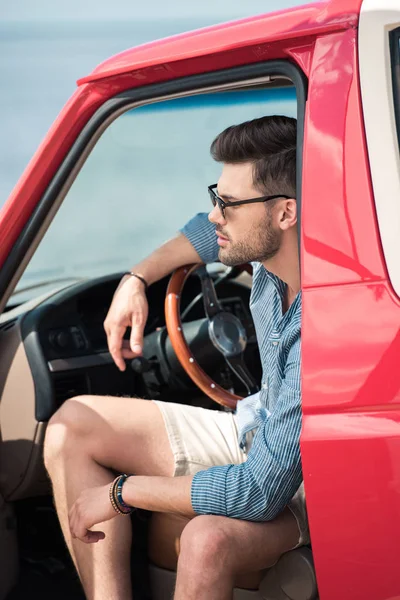 Jovem bonito em óculos de sol sentado em carro vermelho — Fotografia de Stock