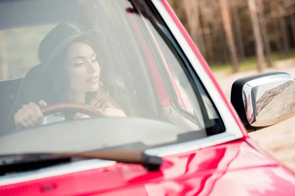 Attractive girl in hat driving car during road trip — Stock Photo