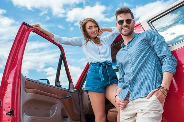 Beautiful happy couple standing near red car — Stock Photo