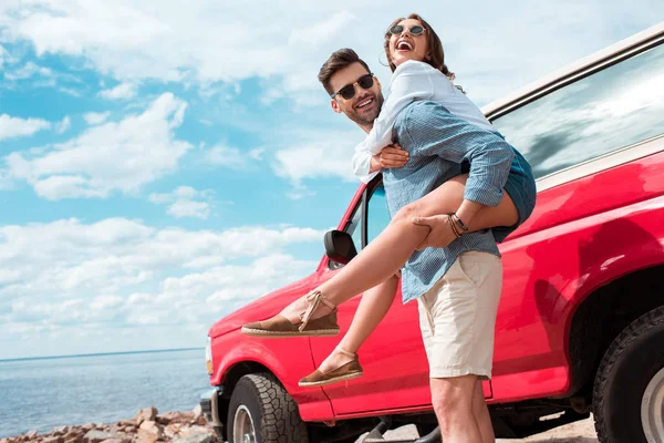Jeune homme piggyback son excité copine près de rouge jeep — Photo de stock