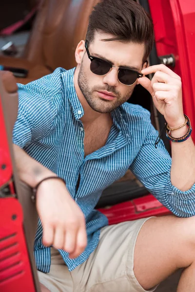 Bel homme élégant dans des lunettes de soleil assis dans la voiture — Photo de stock