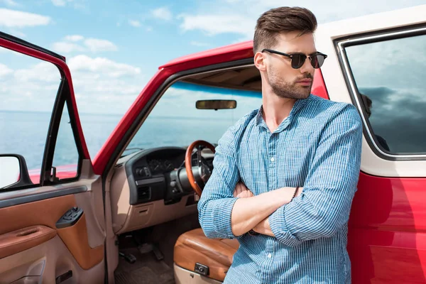 Красивый стильный мужчина-путешественник, стоящий у красной машины у моря — стоковое фото