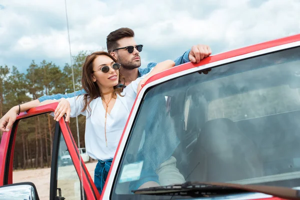 Couple of travelers in sunglasses standing near red car — Stock Photo