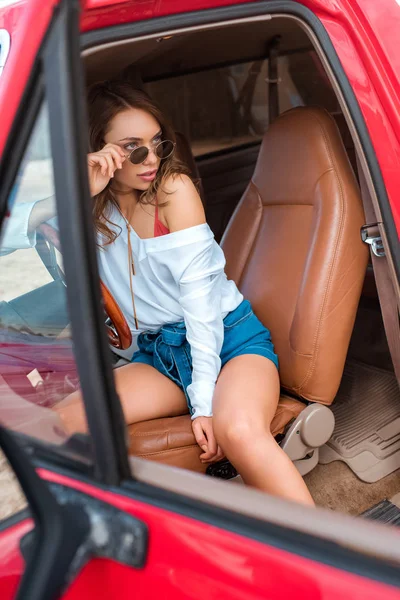 Belle jeune femme en lunettes de soleil assis en voiture pendant le voyage — Photo de stock
