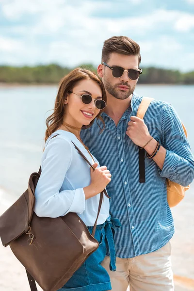 Hermosa pareja sonriente de viajeros en gafas de sol con mochilas - foto de stock