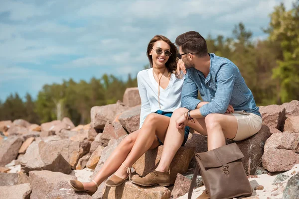 Joven pareja sentado juntos en rocas fuera - foto de stock