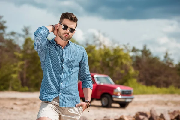Guapo hombre elegante en gafas de sol, jeep rojo en el fondo - foto de stock