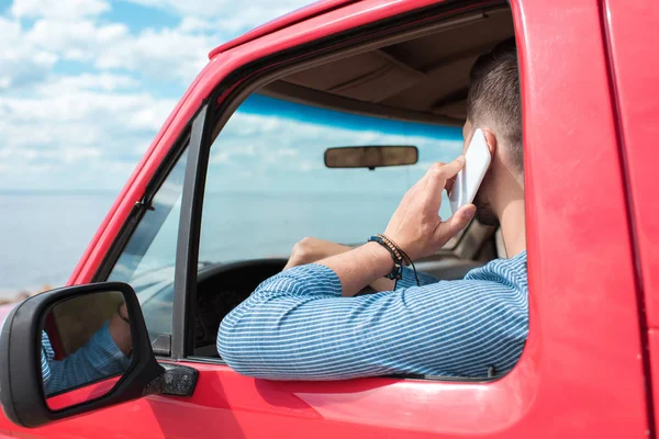 Junger Mann telefoniert während Autofahrt mit Smartphone in rotem Auto — Stockfoto