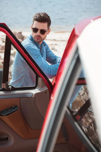 Schöner, stylischer Mann, der während einer Autofahrt am Meer steht — Stockfoto