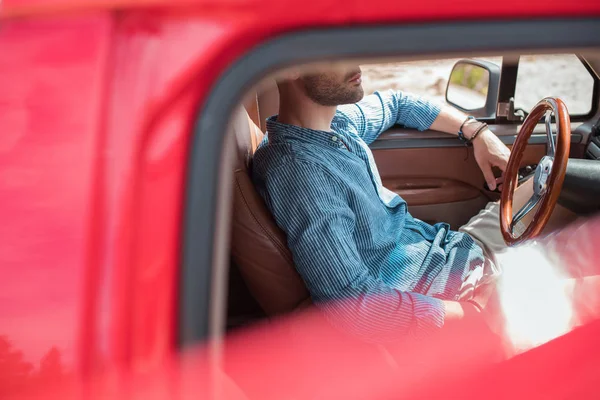 Selective focus of young man sitting in red car during road trip — Stock Photo