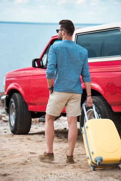 Giovane con valigia gialla che va in jeep rossa vicino al mare — Foto stock