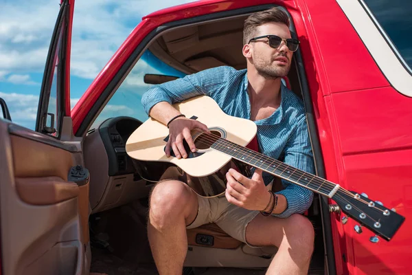 Jovem bonito tocando guitarra acústica no carro durante a viagem de carro — Fotografia de Stock