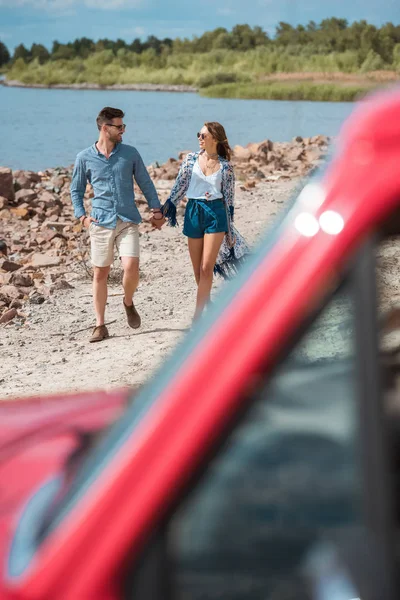 Selective focus of couple holding hands and walking on shore near the sea during road trip — Stock Photo