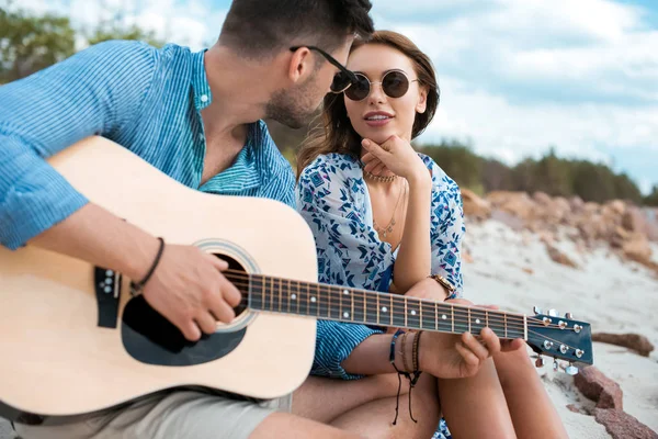 Guitarrista masculino tocando guitarra acústica e sentado com namorada ao ar livre — Fotografia de Stock