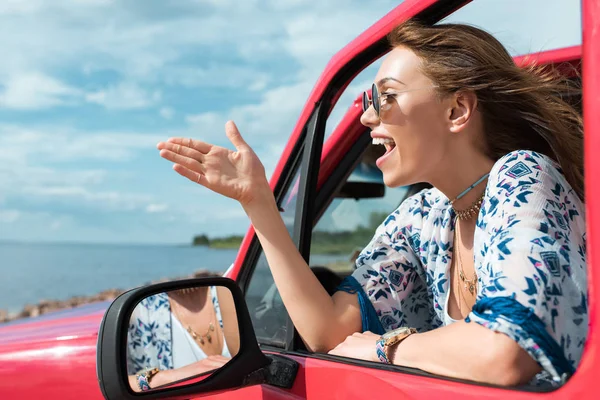 Alegre joven mujer haciendo gestos y hablando en coche durante el viaje - foto de stock