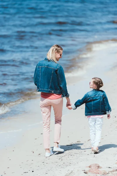 Rückansicht von stilvoller Mutter und Tochter, die sich an den Händen halten und am Ufer gehen — Stockfoto