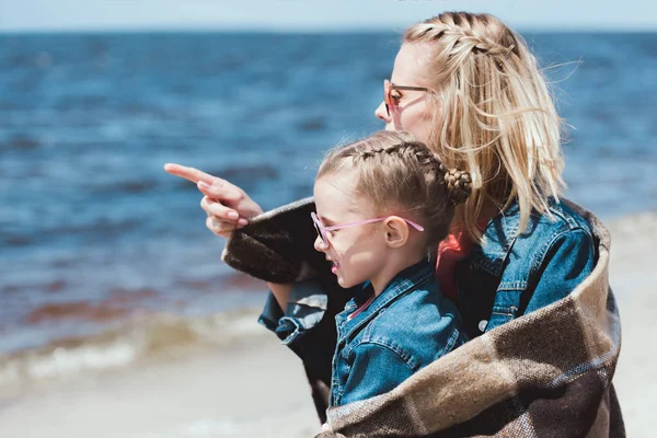 Stylische Mutter und Kind mit Sonnenbrille, die auf das Meer zeigt — Stockfoto