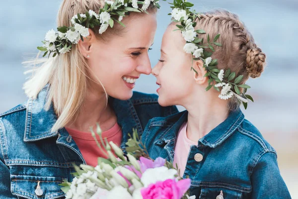 Feliz madre e hija en coronas florales tocando narices - foto de stock