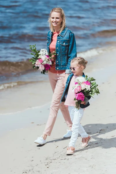 Mère et fille marchant avec des bouquets de pivoines sur le bord de la mer — Photo de stock