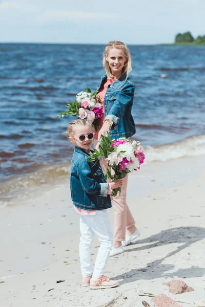 Мати і дочка з піоновидними букетами тримають руки на морському березі — стокове фото