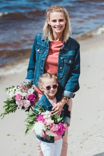 Mother and daughter with peony bouquets on sea shore — Stock Photo