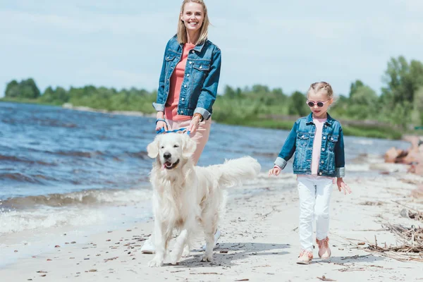 Família feliz andando com cão retriever dourado na costa do mar — Fotografia de Stock