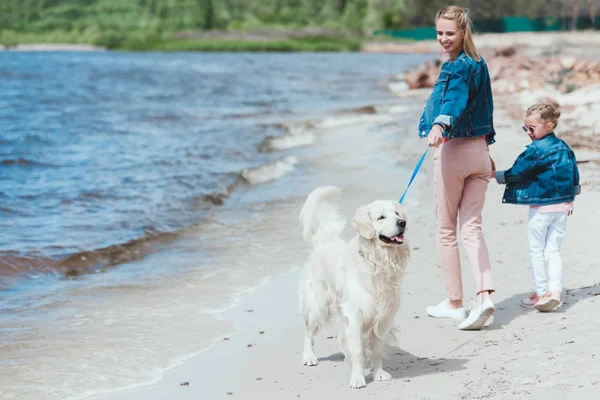 Happy mother and daughter walking with golden retriever dog on sea shore — Stock Photo