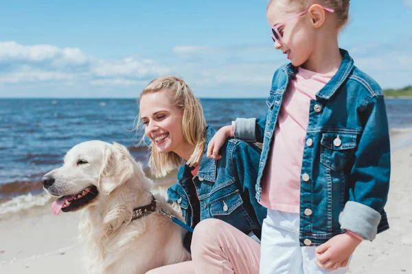 Hermosa familia con perro golden retriever cerca del agua - foto de stock