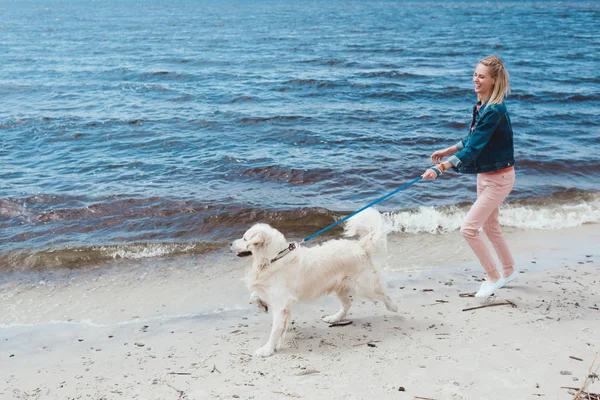 Attractive happy woman walking with dog on sea shore — Stock Photo